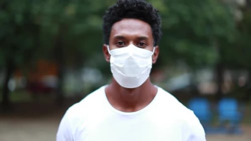 Black African person portrait face wearing surgical pandemic mask outside at park