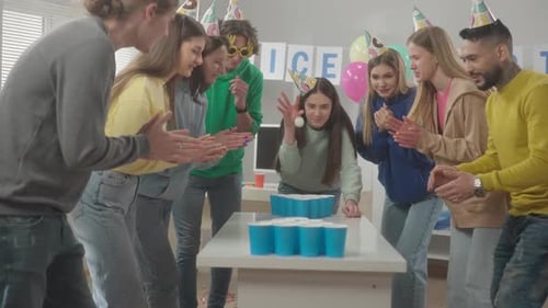 Office Workers in Holiday Hats Have Fun Playing Beer Pong A Young Woman Takes Aim Throws a Ball and