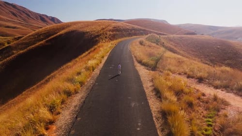 Woman Walks Along a Winding Road in the Highlands of Madagascar The Surrounding Landscape is Arid
