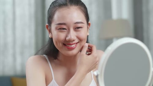 Close Up Of Asian Woman Looking In The Mirror And Smiling After Applying Makeup At Home