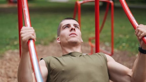 Athletic man doing pull-ups at red sports facility in park