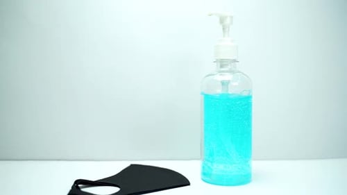 Close up bottle of blue sanitize gel with one hand bring different style of face masks on the table.