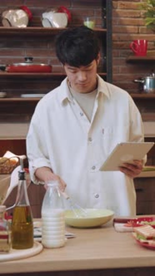 Young Adult Prepares Food in Kitchen with Tablet