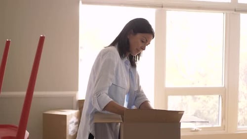 Woman packing cardboard box with items in home