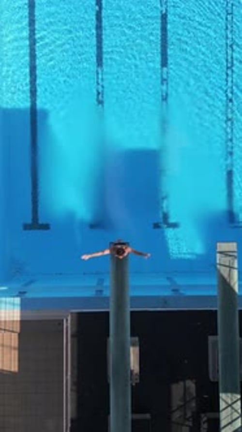 Drone Footage Capturing a Diver Midair Performing a Tuck Dive Above a Clear Blue Pool with Stunning