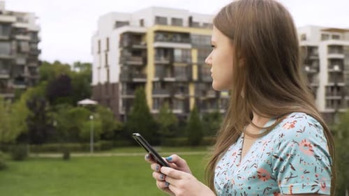 A Beautiful Young Caucasian Woman Works on a Smartphone in a Suburban Area Side Closeup