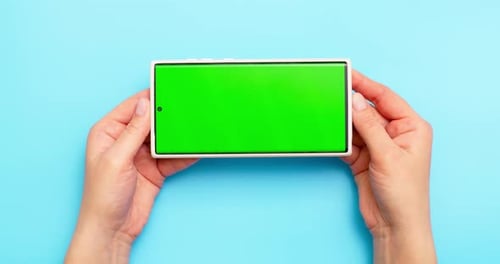 Woman's Hands Holding Smartphone with Green Screen on Blue Background