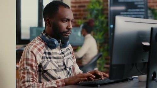 Afroamerikanischer Programmierer codiert auf dem Bildschirm, während kabellose Kopfhörer verwendet werden