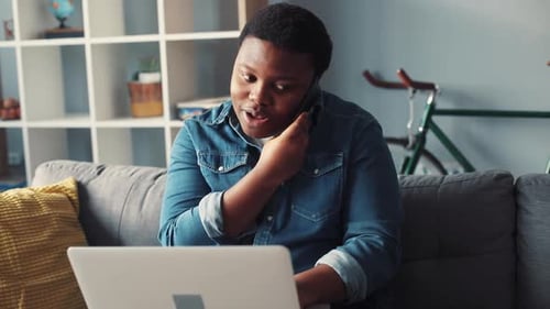 Young Man on Phone Working with Laptop at Home