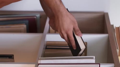 Man Reads Book from Bookshelf at Home
