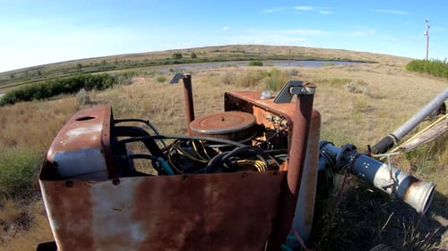 Old farming water pump sitting in a field in the country on a sunny day.
