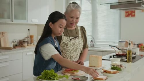 Girl and Grandmother Making Sandwiches Together in Kitchen