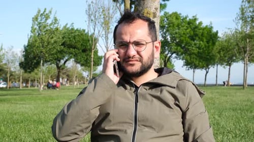 Man Talking on Phone Sitting in Park on Sunny Day