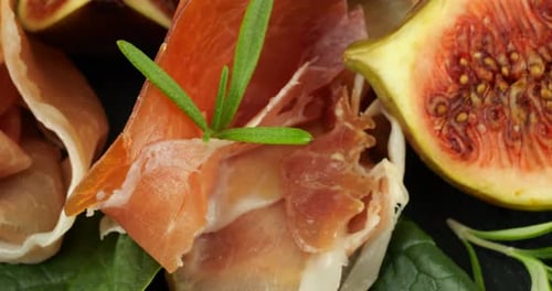 Figues, jamon et feuilles d'épinards sur une planche de service en pierre noire. Set de snacks.