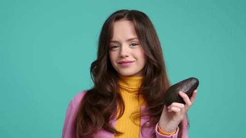 Foto de closeup de uma garota em roupas coloridas segurando abacate fresco e saboroso