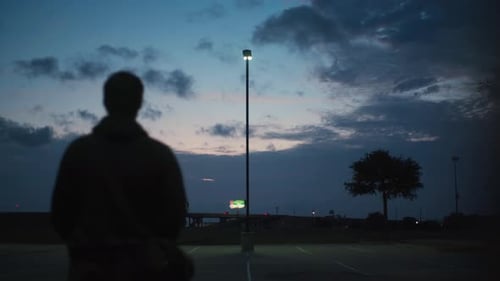 An onlooker watches a distant highway in a quiet parking lot.
