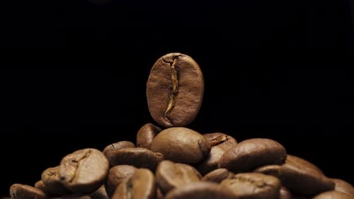 One coffee bean on a black background rotates on top of a stack of coffee beans. Close-up, blinking