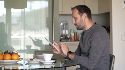 Man Uses Tablet at Kitchen Table at Home