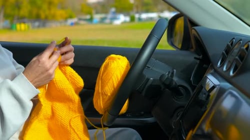 Woman Knitting Bright Yellow Yarn Inside of Car