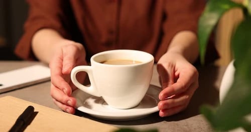 Woman taking cup of delicious coffee at grey textured table in cafe, closeup