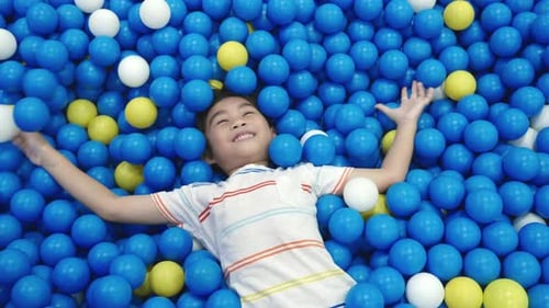 Happy Asian child man having fun on entertainment center inflatable castle in balls sea