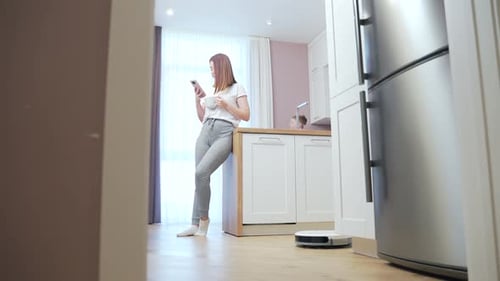 woman enjoys a robot vacuum cleaner. Young female is resting while cleaning the house. controls