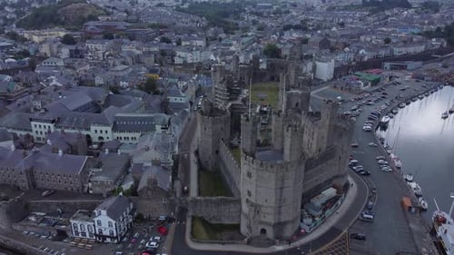 Ancient Caernarfon castle Welsh harbour town aerial view medieval waterfront landmark slow descendin