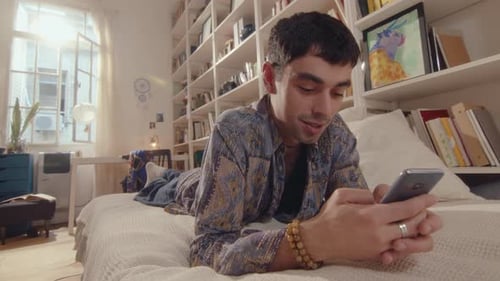 Young Adult Lying on Bed Using Phone