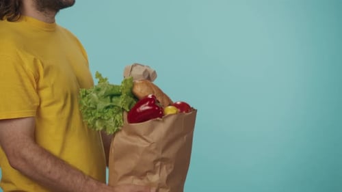 Closeup Shot Delivery Man in Yellow Uniform Giving a Paper Bag with Grocery Food Products to Client