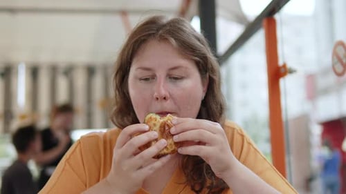 Pensive Plus Size Woman Bites and Chews Fatty Fried Flatbread in Street Cafe