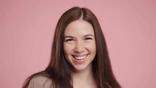 Smiling Woman Winks and Laughs Against Pink Backdrop