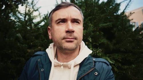Portrait d'un homme regardant loin de la caméra, encadré par des sapins verts denses, avec du natu doux