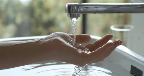 Water Flowing From Faucet Over Hand in Sink