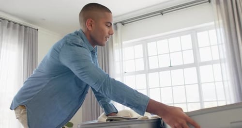 Young Man Packing Suitcase on Bed for Travel
