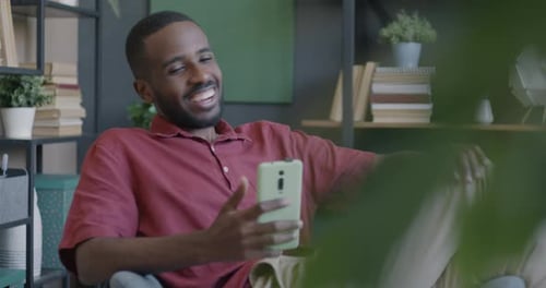 Man Smiling Using Smartphone Video Call in Armchair