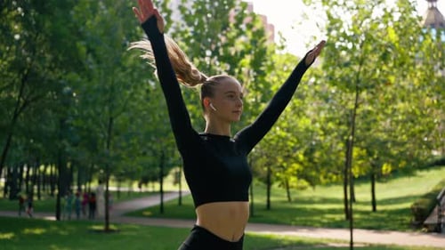 A girl athlete performs jumping exercises as a warm-up before training on the street in green park