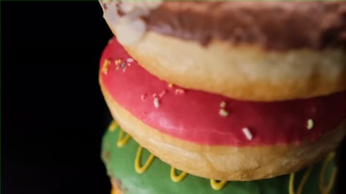 Grande pile de beignets délicieux avec un glaçage de différentes couleurs et des paillettes sur fond noir.