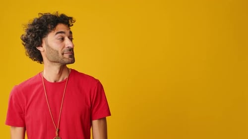 Surprised man looks to side to show copy-space isolated on yellow background in studio