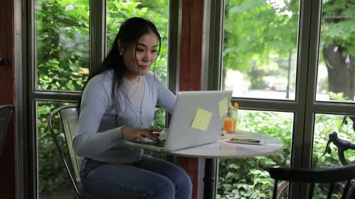 Young Asian woman working in coffee shop using laptop.