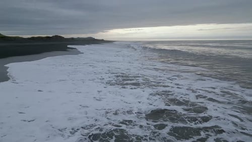 Low and fast-flying drone flies over large surf waves crashing onto the black sand. ICELAND.