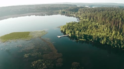 Drone Flies Over a Huge Blue Lake with Long Wooden Pier and Boat Among Forests