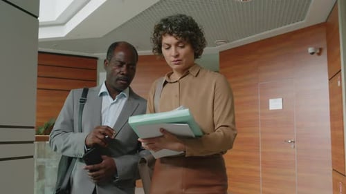 Business Partners Discussing Documents Walking in Office Corridor
