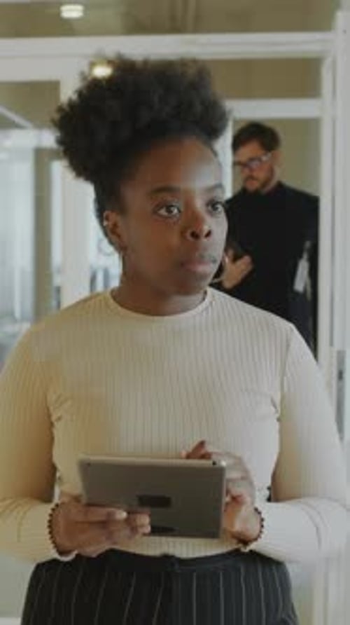 Young Black Businesswoman Walking in Office Corridor and Using Digital Tablet