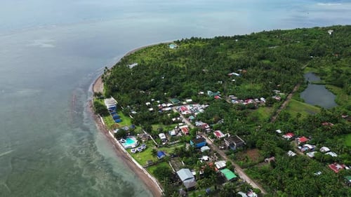 Stunning overhead view of rural, island village with lush jungles facing clear ocean coastline in Ca