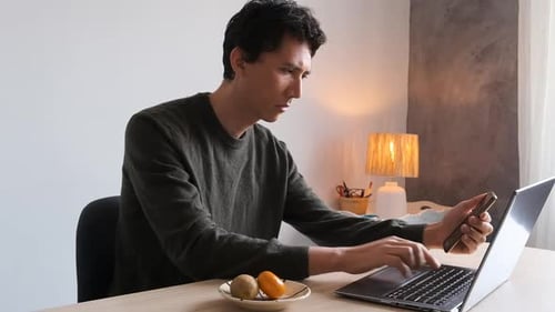 Man Using Laptop and Smartphone at Desk Indoors