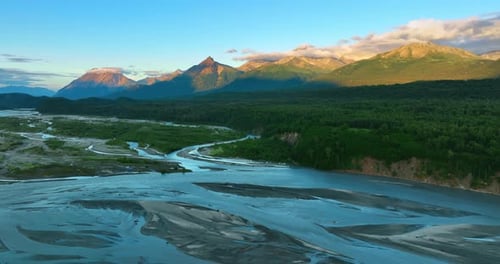 Shallow river flowing the beautiful valley. Setting sun lights the mountain tops partially
