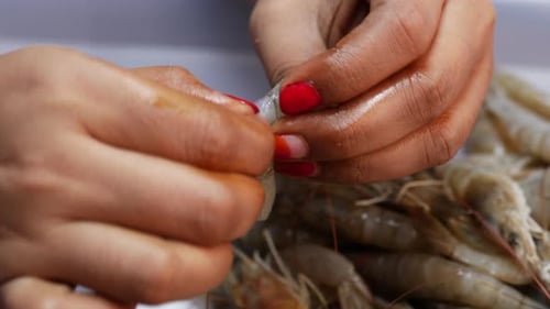 A woman peels shrimp from a string. Close-up of her hands holding the shrimp