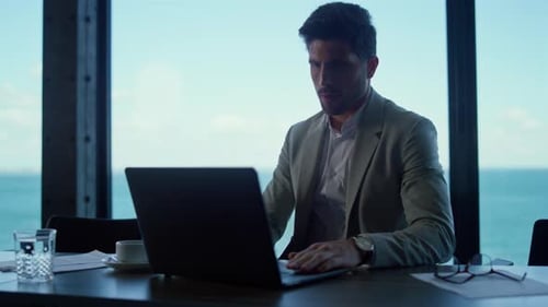 Focused Professional Using Laptop Computer in Sea View Office. Serious Businessman Typing
