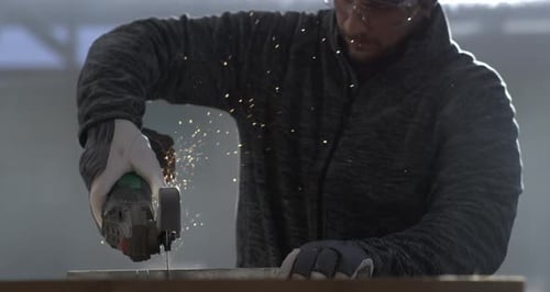 Worker grinding metal with angle grinder, sparks illuminating scene in slow-motion at fps