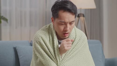 Gros plan d'un homme asiatique avec une couverture souffrant de toux sur le canapé dans le salon à la maison
